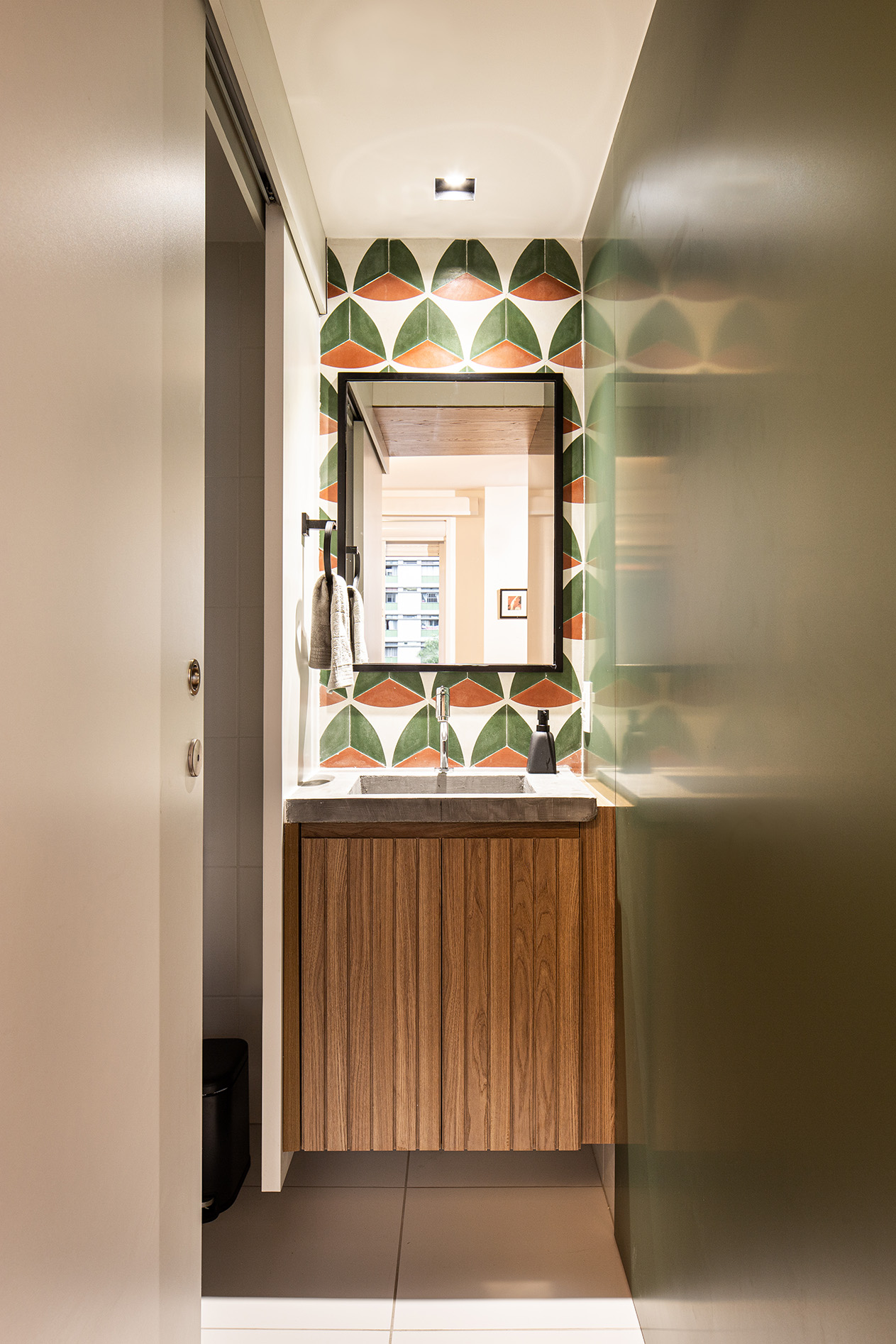 Lavabo com gabinete de madeira, pia de concreto e detalhes no espelho em preto